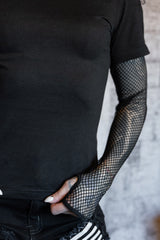 Person wearing a black t-shirt and fishnet sleeves with a blurred background