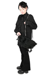 A model wearing a black gothic outfit, including a long-sleeve button-up shirt, flared pants, and black boots, carrying a black raven-shaped shoulder bag with a silver chain strap against a solid white background.