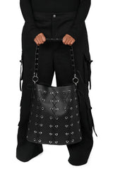 Black studded handbag held by a person wearing black clothing on a white background