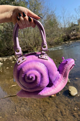 Purple snail-shaped handbag held by a person with a natural background