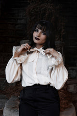 Woman wearing a white edwardian blouse with puffed sleeves in a dark, rustic setting