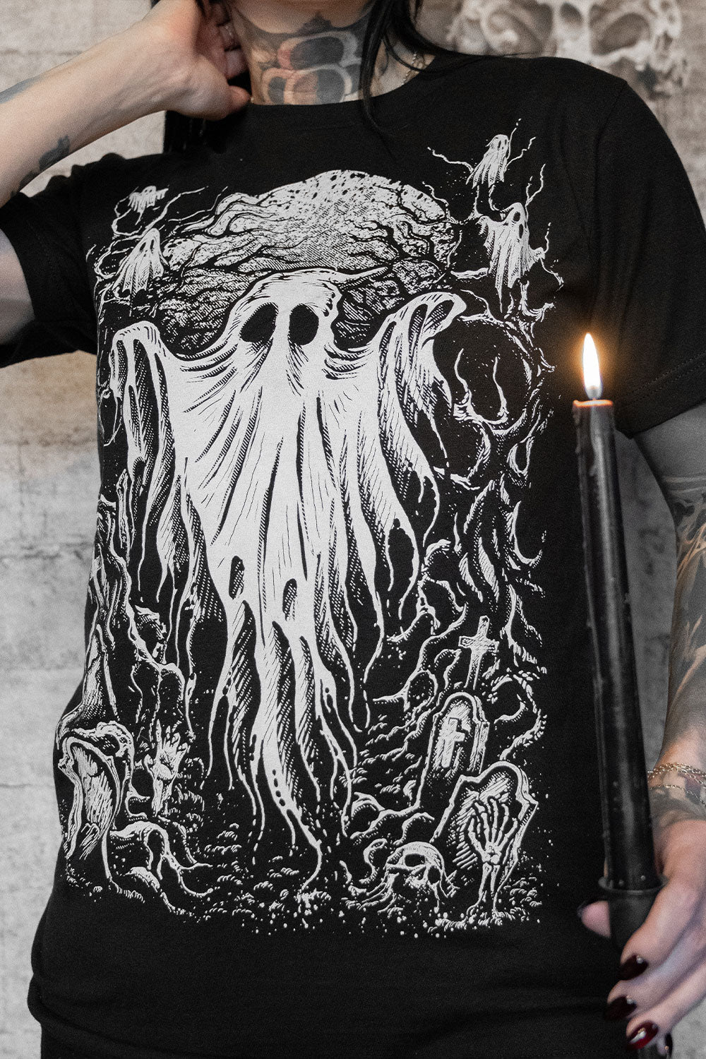 Person wearing a black t-shirt with a white graphic design of a ghostly figure and candles.