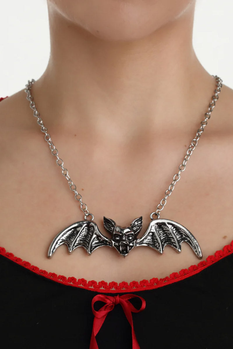 Silver bat necklace on a person wearing a black top with red lace details.