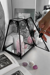 Decorative goth glass box with black metal frame on a white surface with candles and crystals.