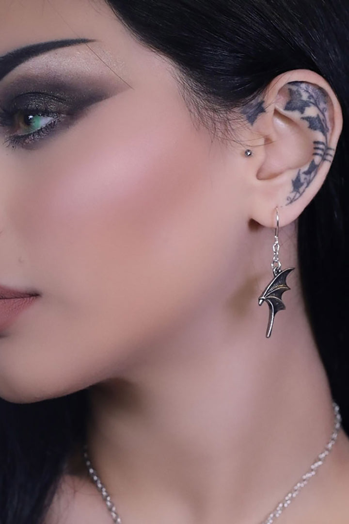 Close-up of a woman's ear with a bat-shaped earring and visible tattoos.