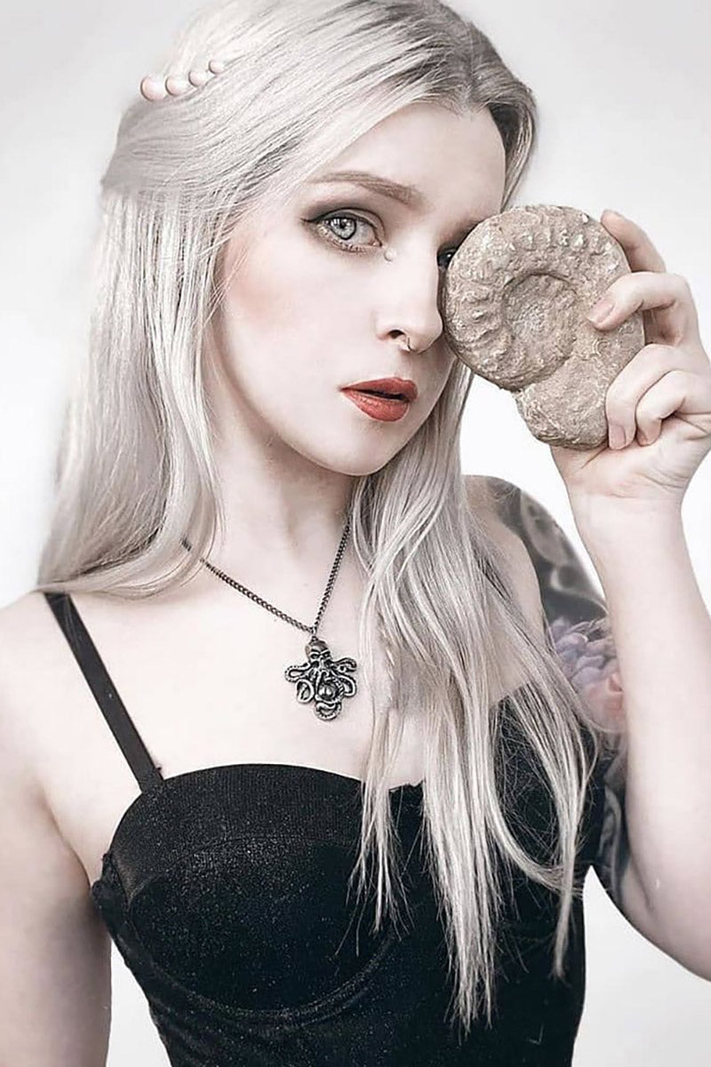 Woman with long blonde hair wearing a tentacle necklace against a white background