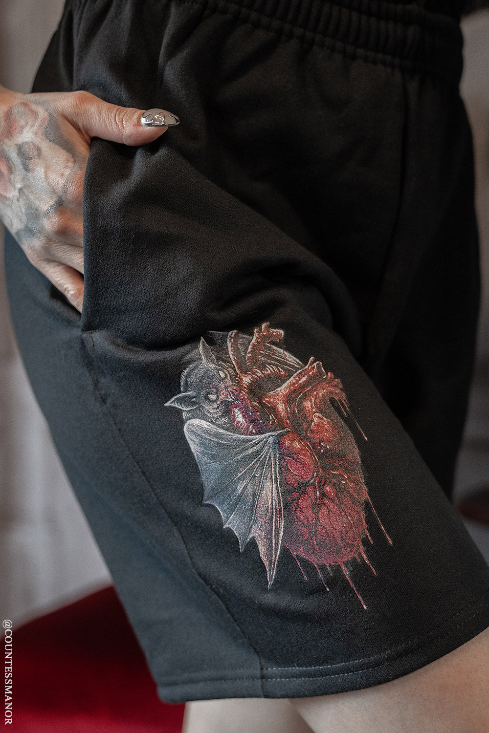 Close-up of a person wearing black sweat shorts with a printed bat and bloody heart design on the side.
