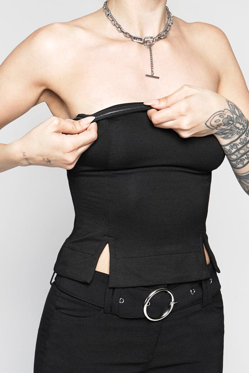 Person wearing a black strapless top and pants with a belt, on a plain background