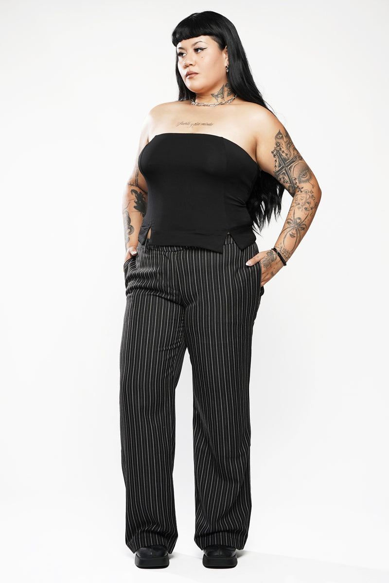Woman wearing a black strapless top and pinstripe pants on a white background