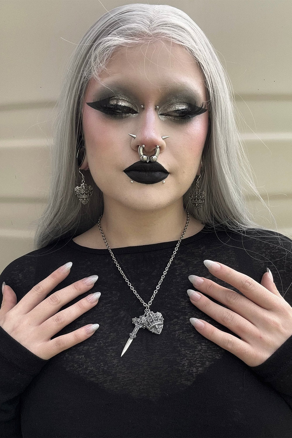 Person with silver hair and dark makeup wearing a black top and gothic jewelry 