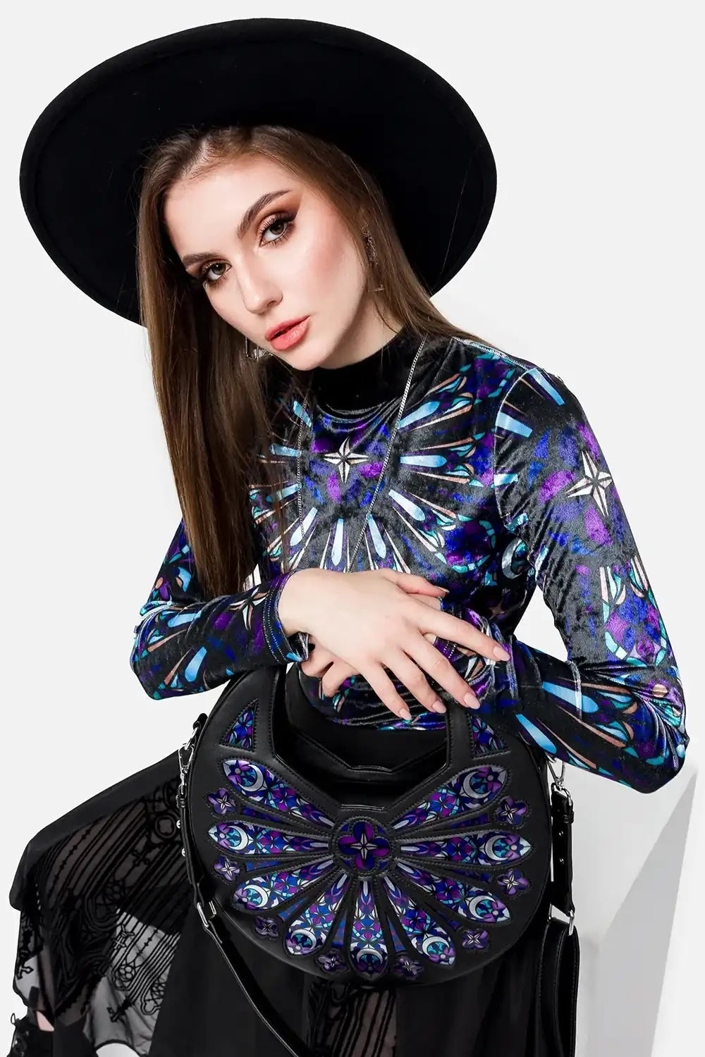 Woman wearing a black hat and a colorful outfit holding a matching handbag against a white background