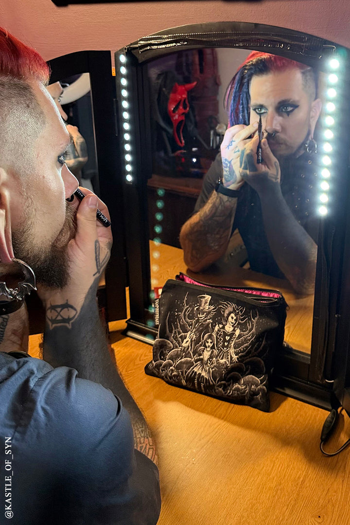 gothic guy putting on makeup beside an emo alice in wonderland makeup bag 