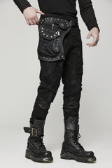 A person wearing a black leg harness bag with distressed pyramid studs and metal skull hardware, featuring zippered pockets, leg and waist straps. The item is hand-painted, and the person is dressed in all black with black boots.