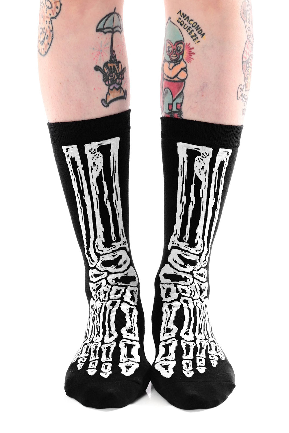 Black socks with white skeleton design worn by a person with tattoos on a white background