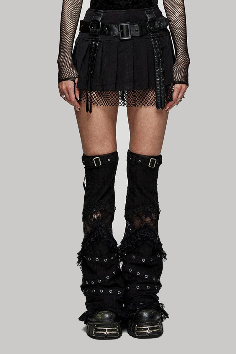 Person wearing a black outfit with a short punk skirt, fishnet stockings, and black knee-high boots on a gray background