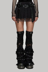 Person wearing a black outfit with a short punk skirt, fishnet stockings, and black knee-high boots on a gray background