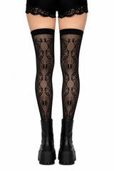 Black gothic thigh-high stockings with a repeating spider pattern, worn with black lace-up platform boots against a white background.