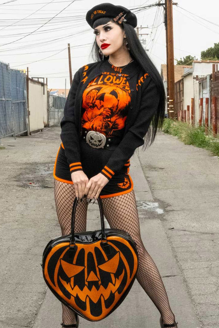 Person wearing a Halloween-themed outfit with a jack-o'-lantern bag on a street.