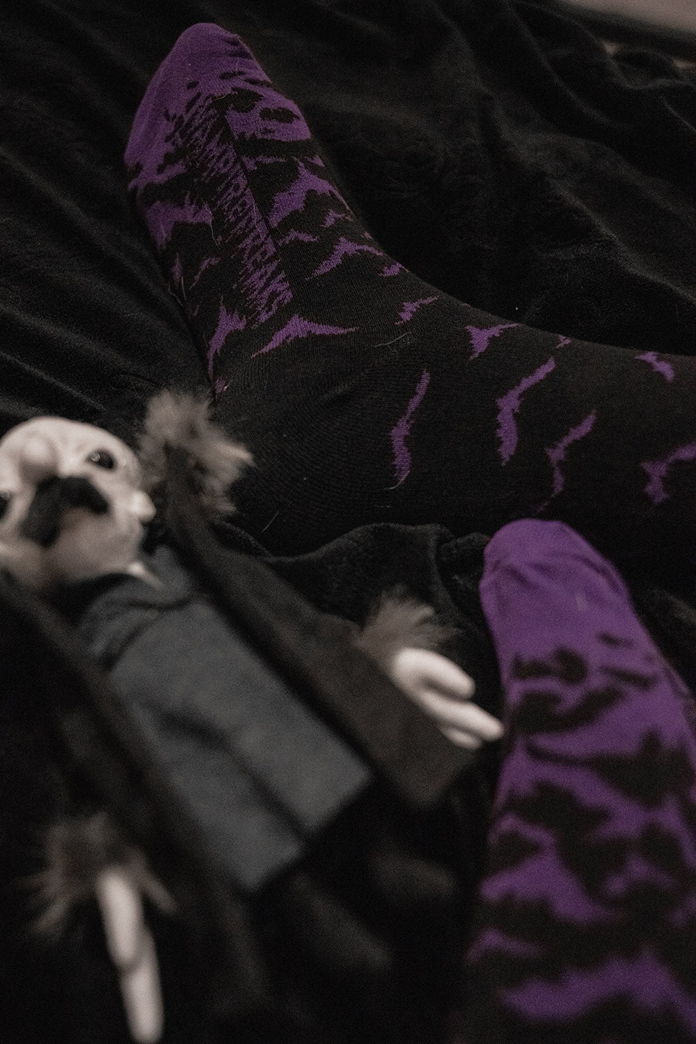 Person wearing purple patterned bat socks sitting on a dark surface with a small vampire doll