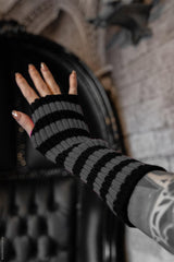 Black and gray striped fingerless gloves worn by a person with tattoos, against a blurred background.