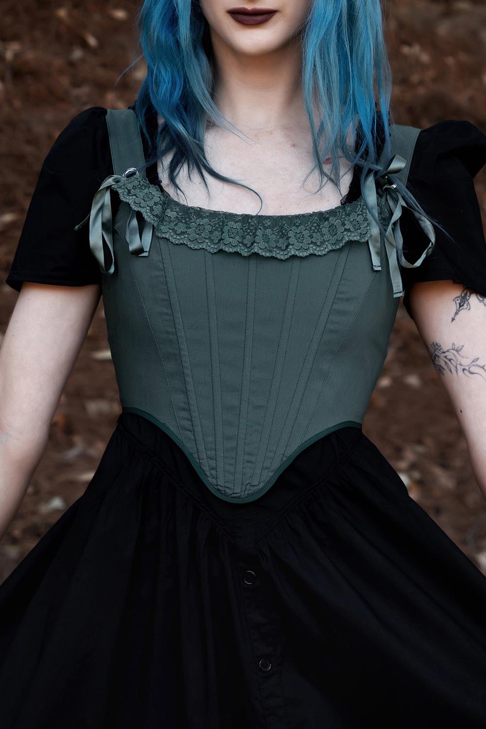 Person wearing a green corset over a black dress with a blurred background