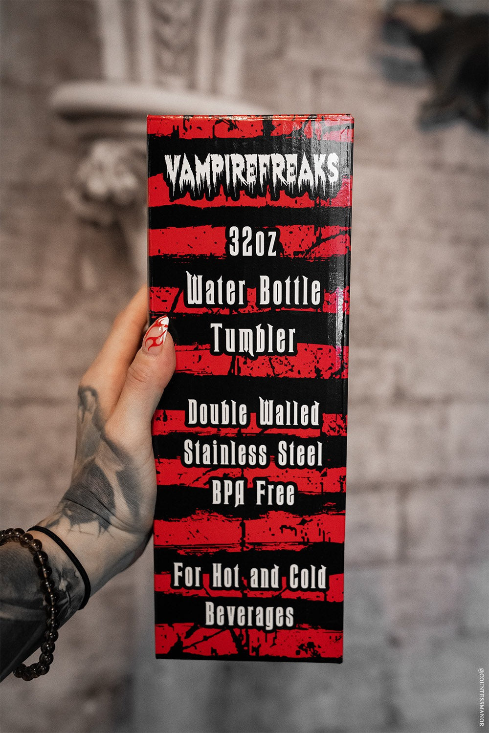 Vampire Freaks water bottle packaging held by a hand with tattoos against a gray stone wall.