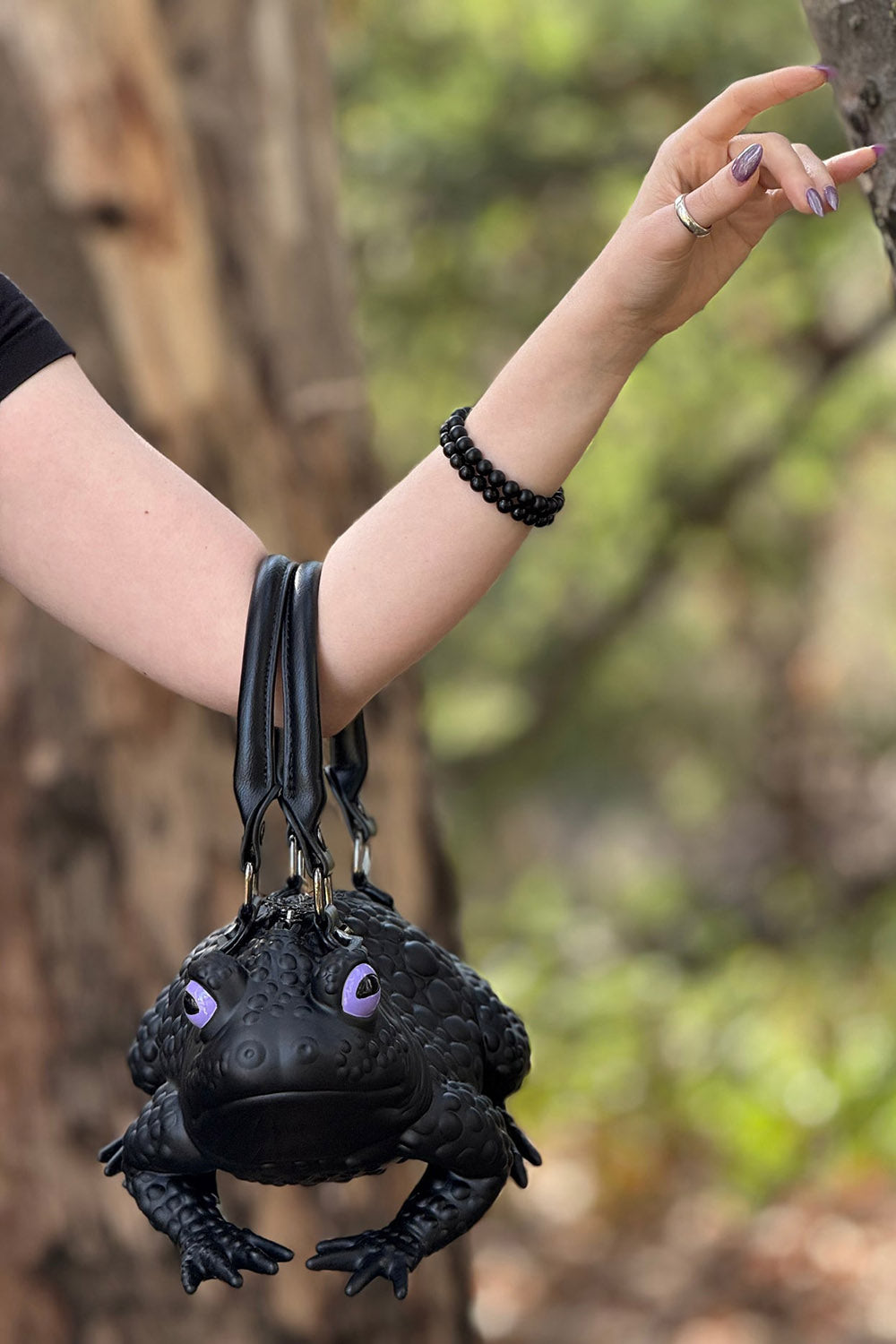 Black frog-shaped bag held by a person in a forest setting