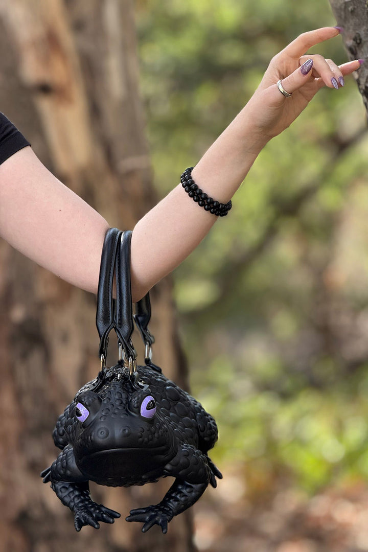 Black frog-shaped bag held by a person in a forest setting
