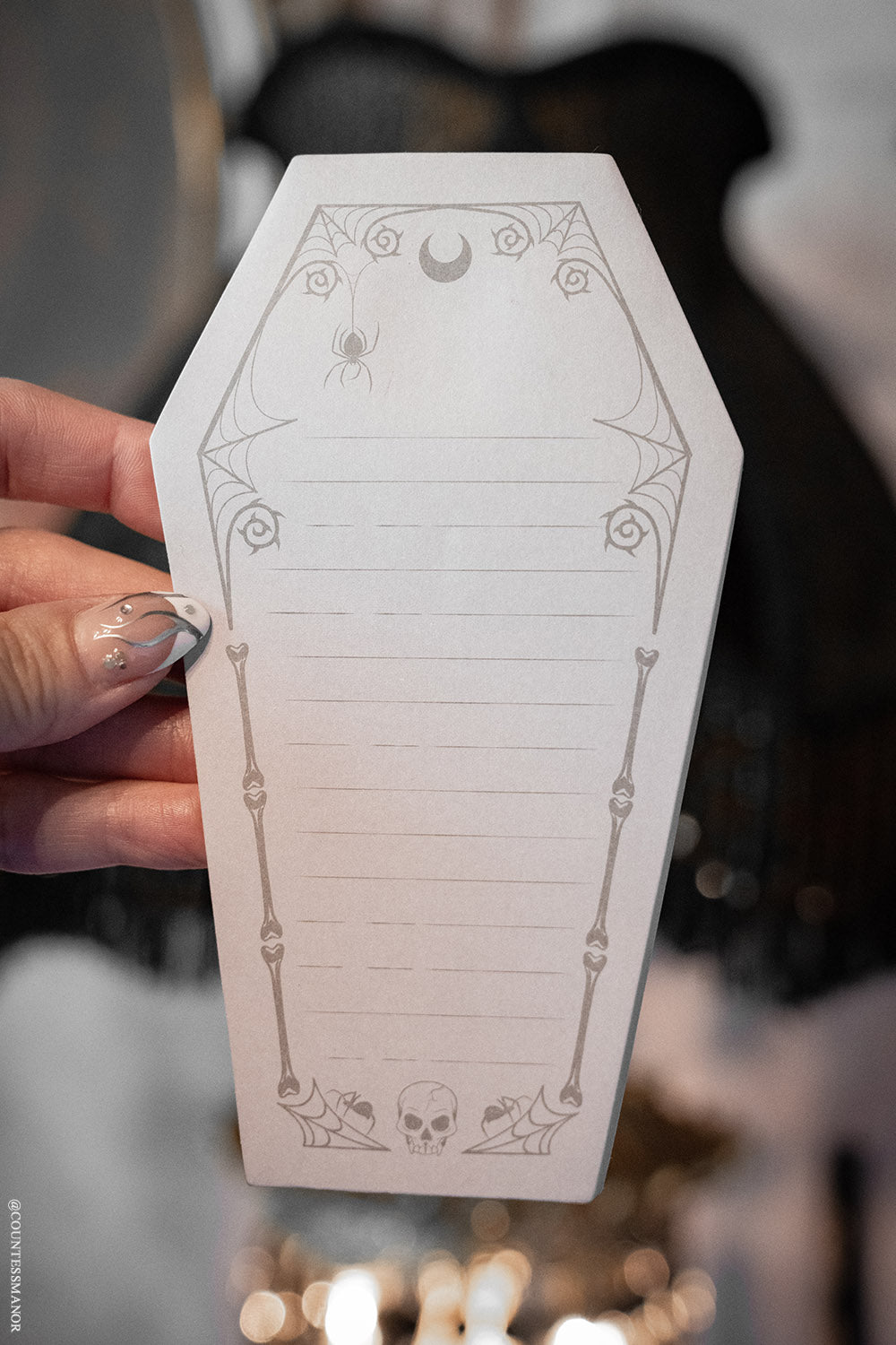 Coffin-shaped notepad with Halloween-themed designs held by a hand.