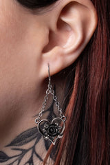 Close-up of an ear wearing a silver heart-shaped earring with a rose design.