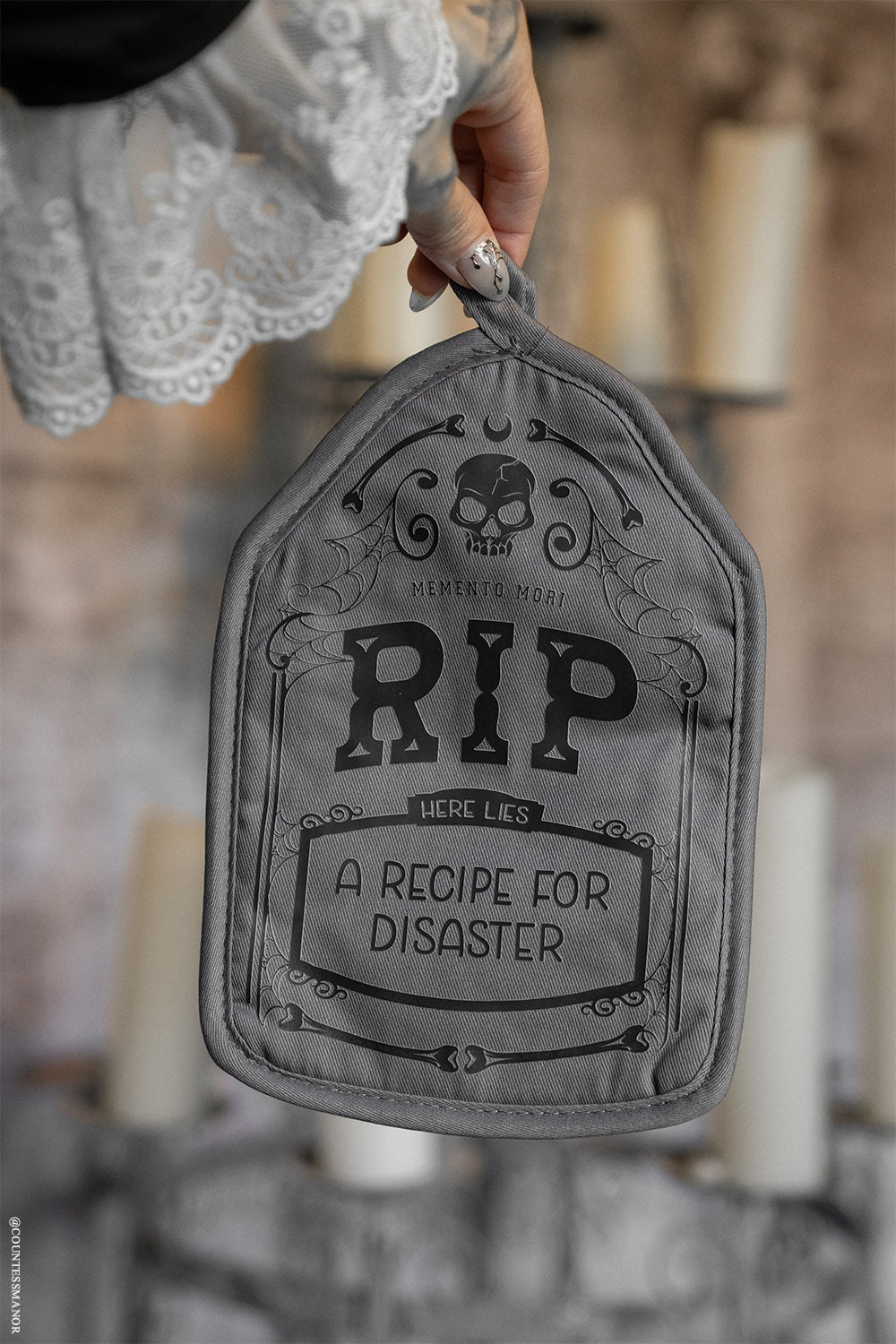 Gray pot holder with 'RIP here lies a recipe for disaster' text held by a person.