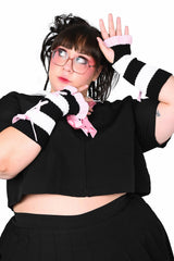 Person wearing a black outfit with striped fingerless ruffled gloves on a white background