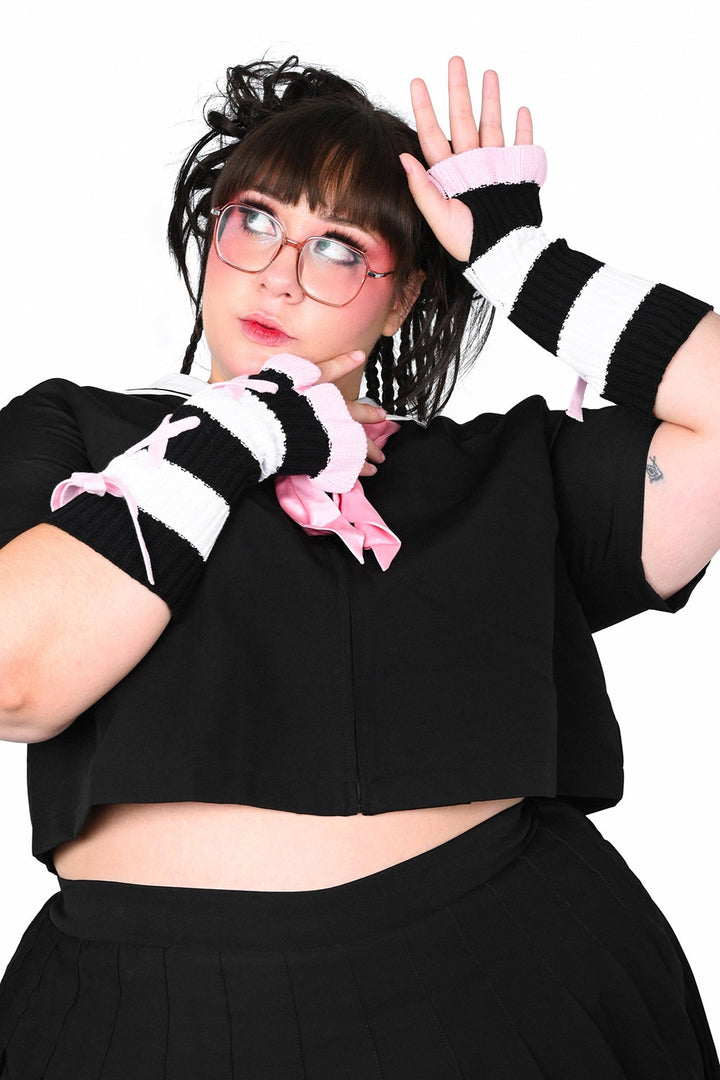 Person wearing a black outfit with striped fingerless ruffled gloves on a white background