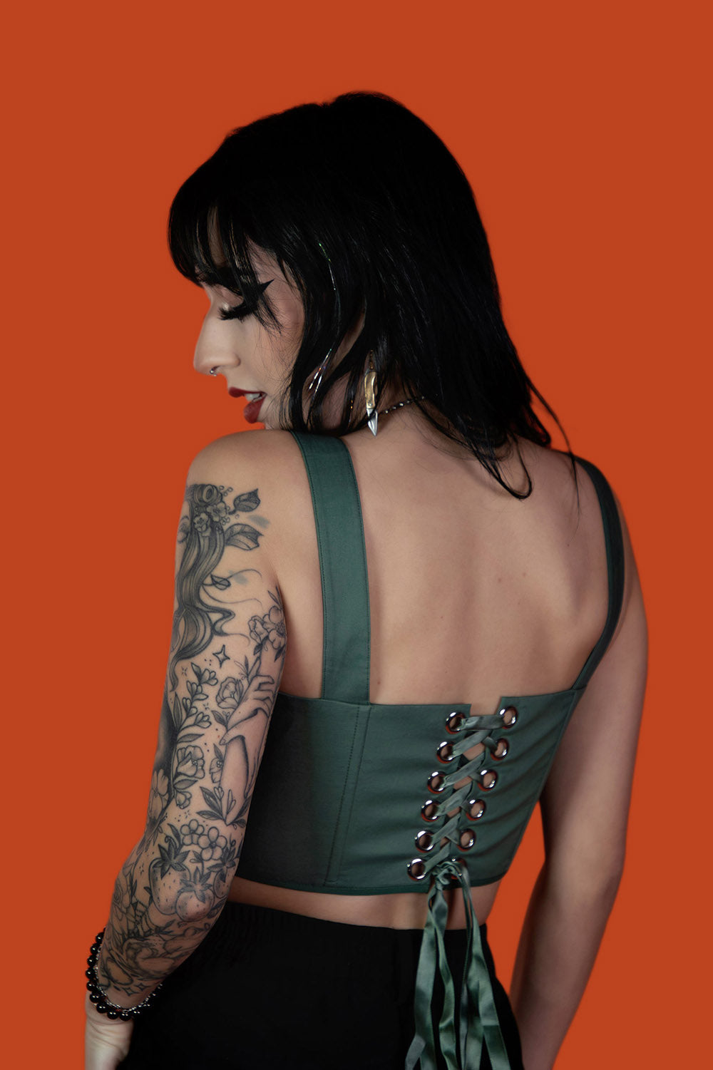 Woman wearing a green lace-up top against an orange background
