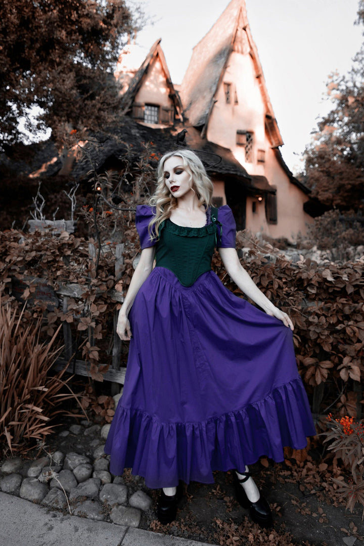 Woman in a purple dress standing in front of a haunted house.