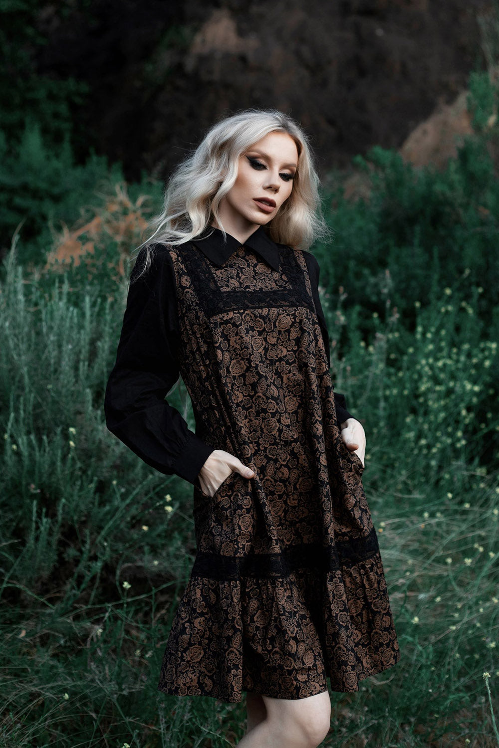 Woman in a black and brown patterned dress standing in a forest setting