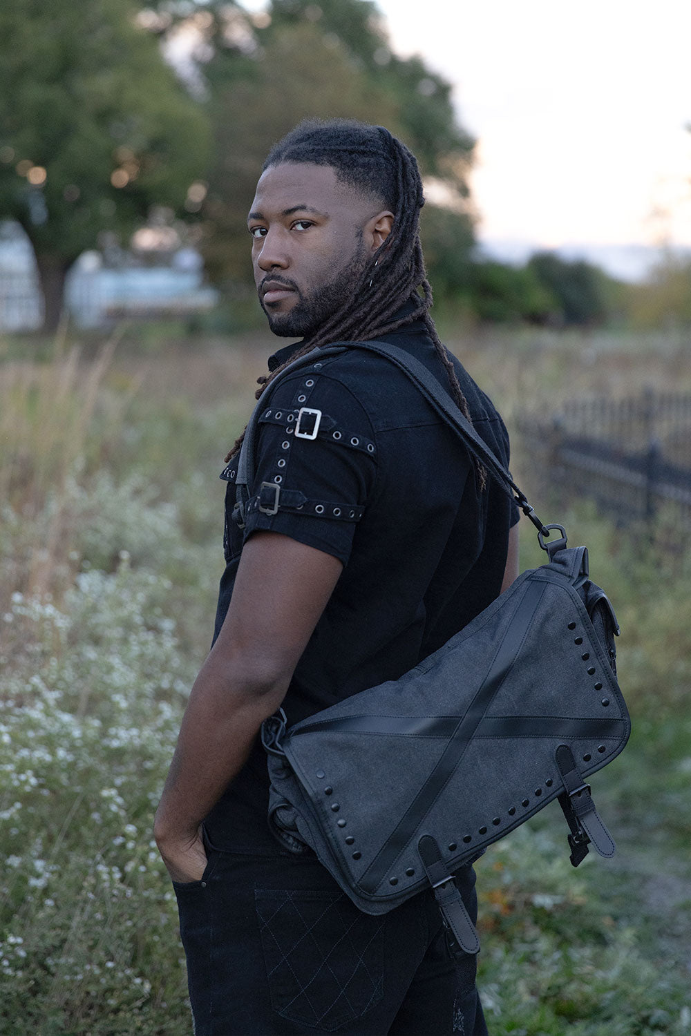 Dark punk messenger bag with distressed grey finish metal studs and utility compartments for industrial goth outfits and rebellious streetwear