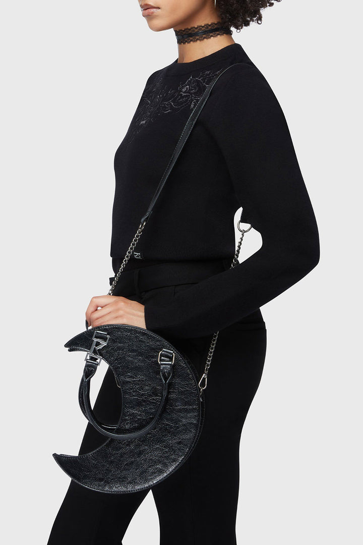 gothic girl wearing a black outfit with a unique 3d novelty moon handbag on a plain background