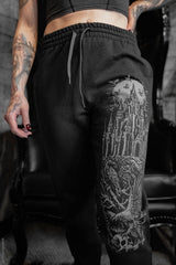 Person wearing black sweatpants with a detailed tattoo design on one leg, standing indoors.