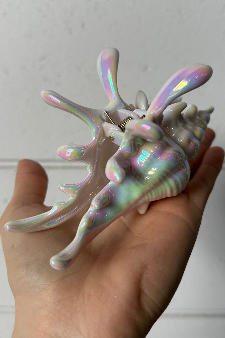 Iridescent shell-shaped hair clip held in a hand against a neutral background