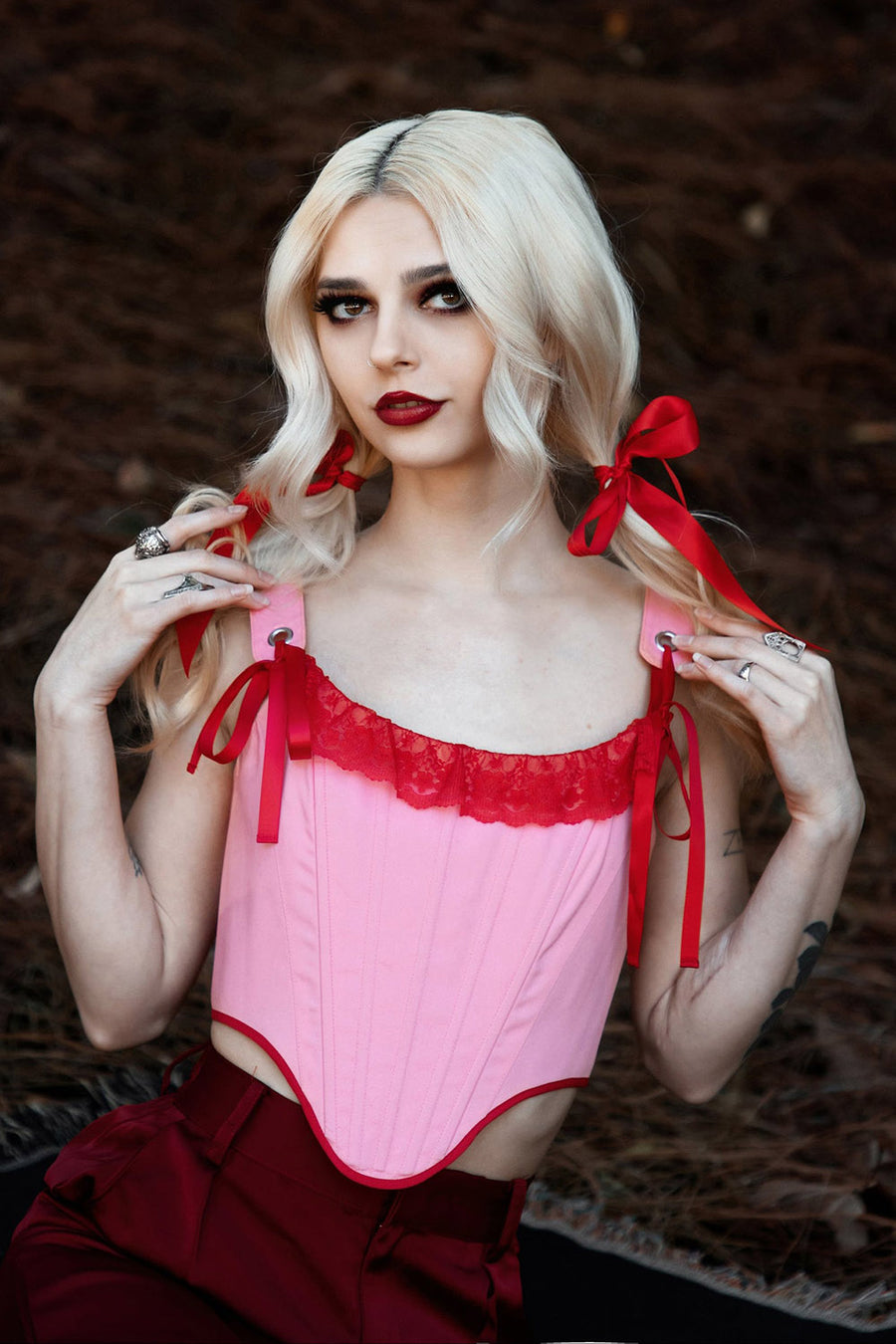 Woman wearing a pink corset with red ribbons against a dark background