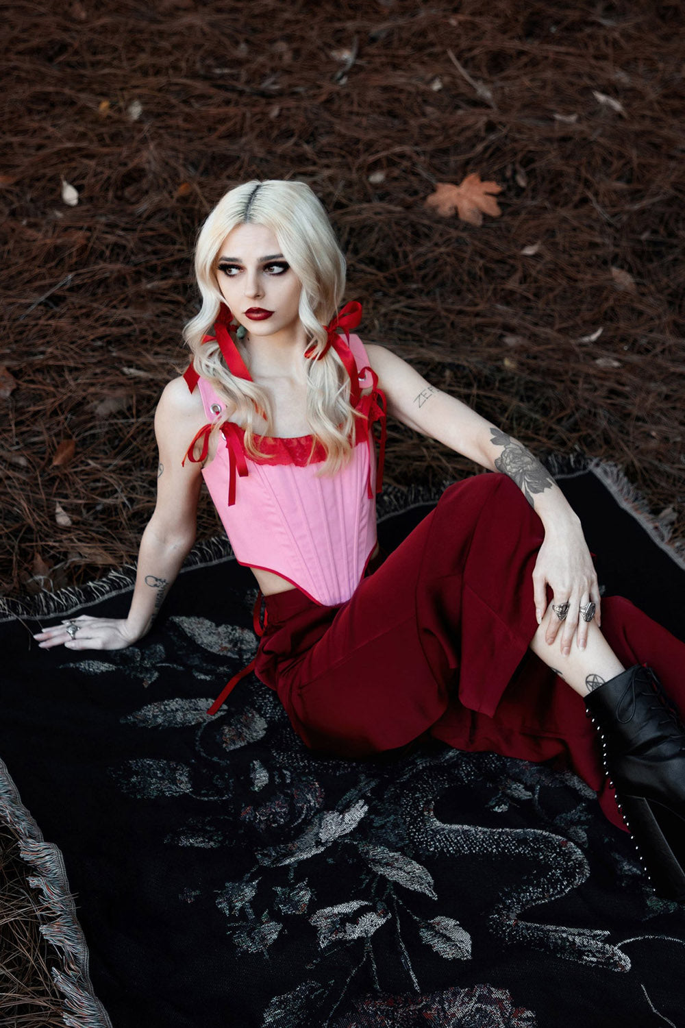 Woman in a pink top and red pants sitting on a textured surface with a dark background