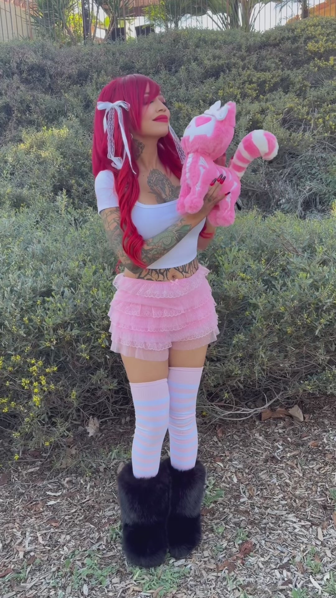 video of a kawaii goth woman holding a emo pastel goth pink skeleton cat plushie toy stuffed animal wearing a bow