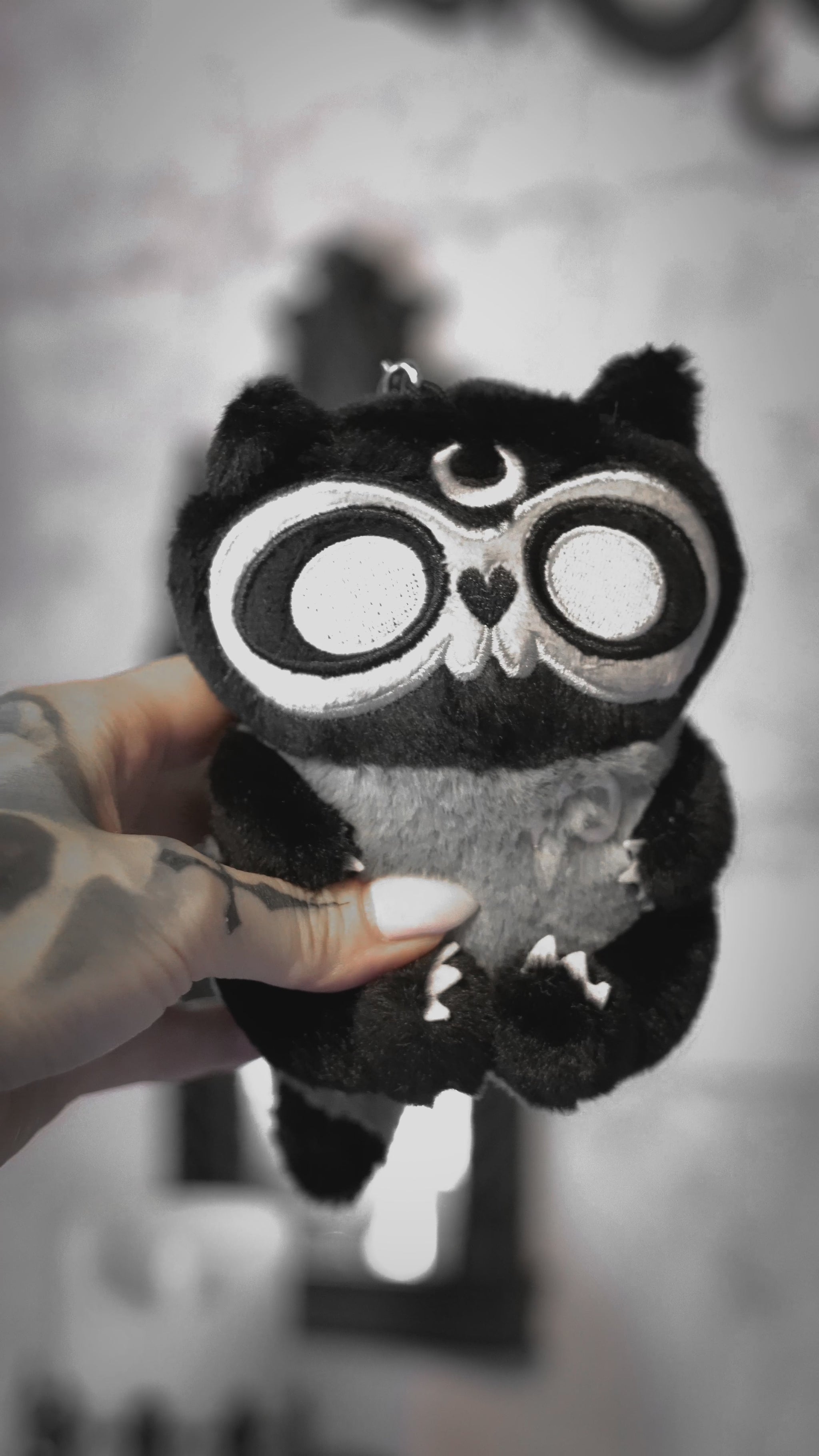 video of a creepy cute stuffed animal raccoon keychain with embroidered moon