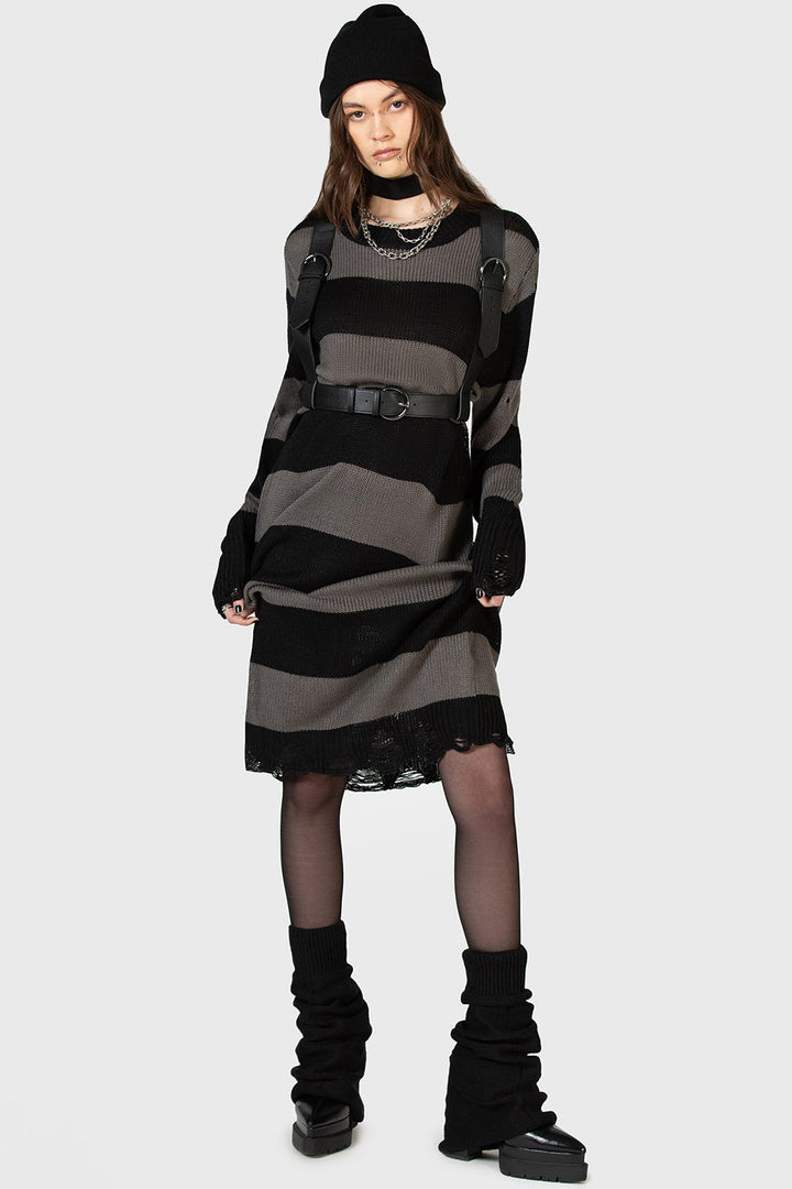 goth girl wearing a black and grunge gray striped dress with a high-waisted punk belted harness, black boots, and a black beanie on a white background.