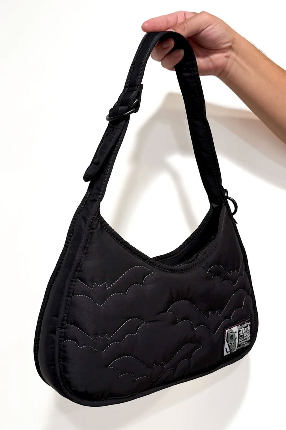 Small black shoulder bag with 2 open interior pockets, 1 interior zipper pocket, top zipper closure, and an adjustable shoulder strap