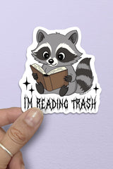 Sticker of a raccoon reading a book with 'I'm Reading Trash' text on a purple background.