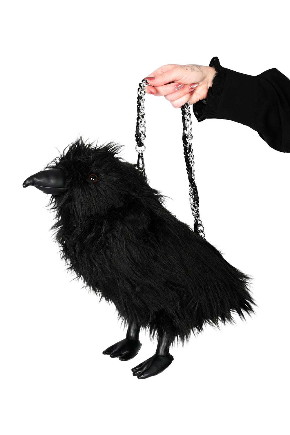 A black raven-shaped fluffy purse with a silver chain strap, held by a hand against a solid white background.