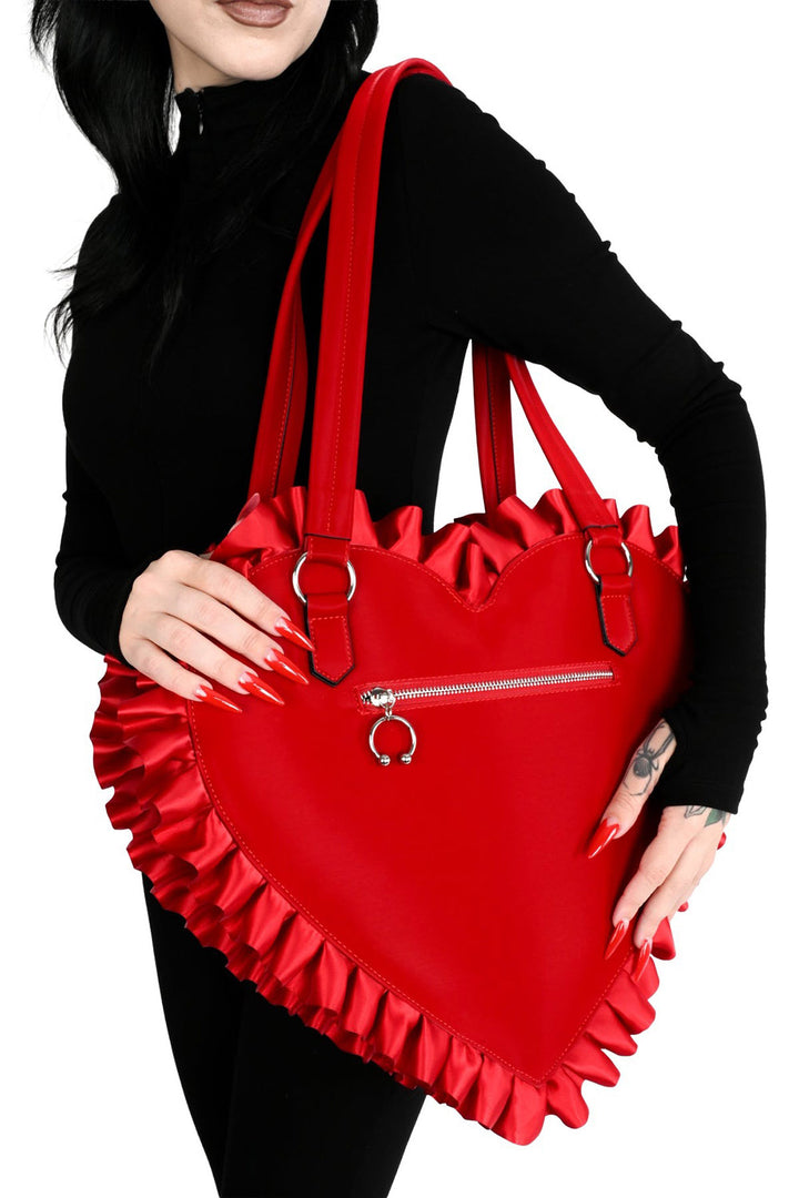 Red heart-shaped bag with ruffles held by a person against a white background
