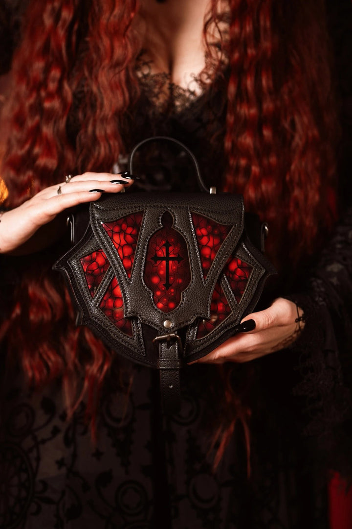 Black handbag with red interior held by a person with red hair.